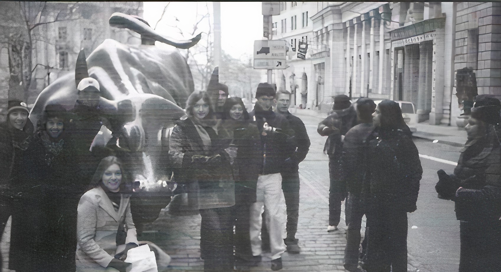Black and white photo of group of people standing by statue of a bull.
