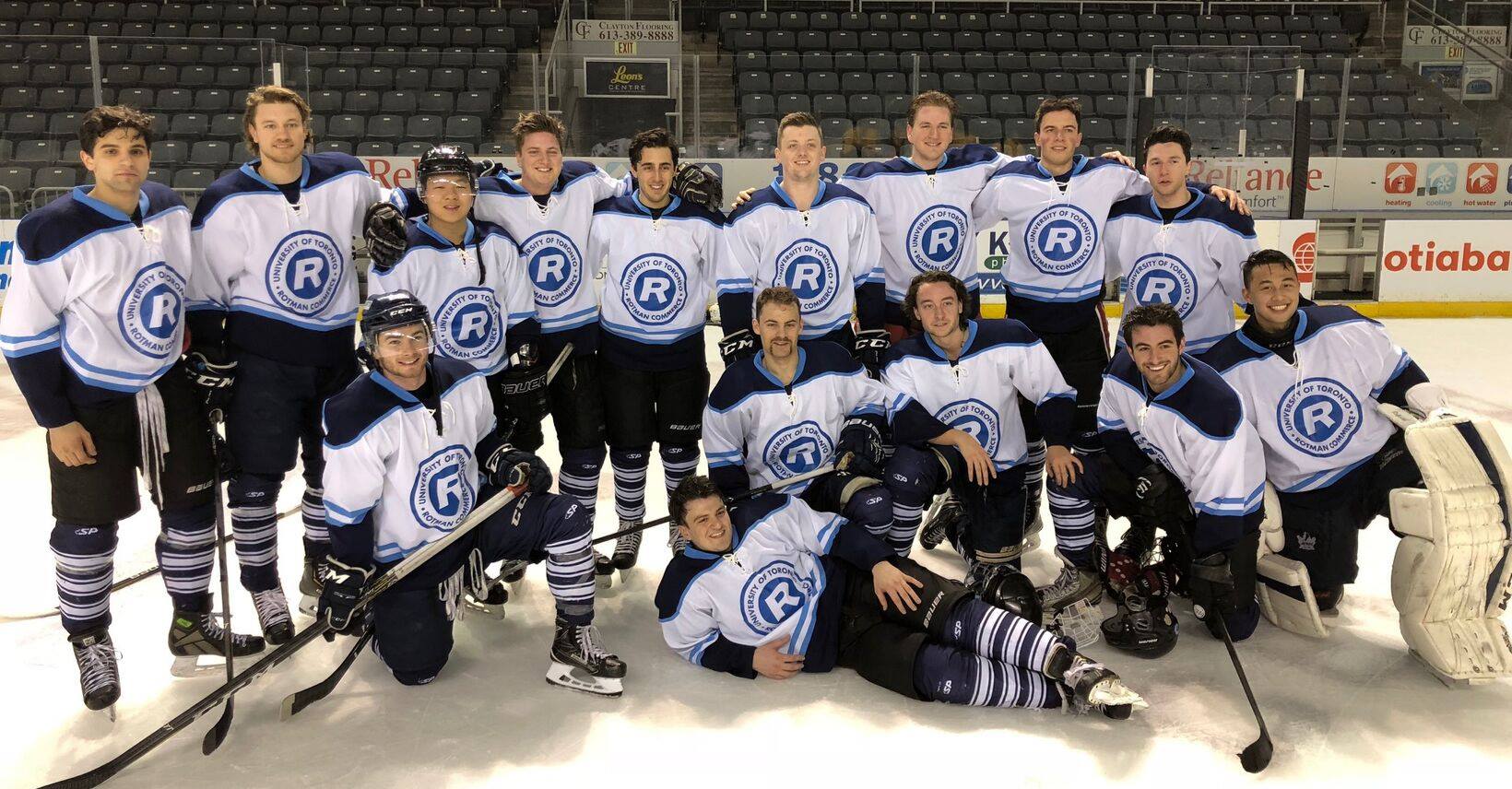 Group of people on an ice rink wearing hockey attire. The jerseys say University of Toronto Rotman Commerce.