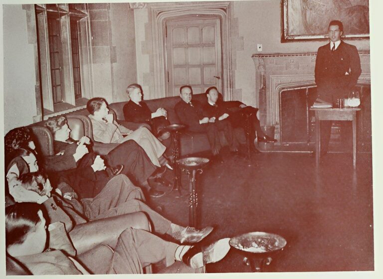 Black and white photograph of Commerce Club members seated on couch, listening to speaker, 1939