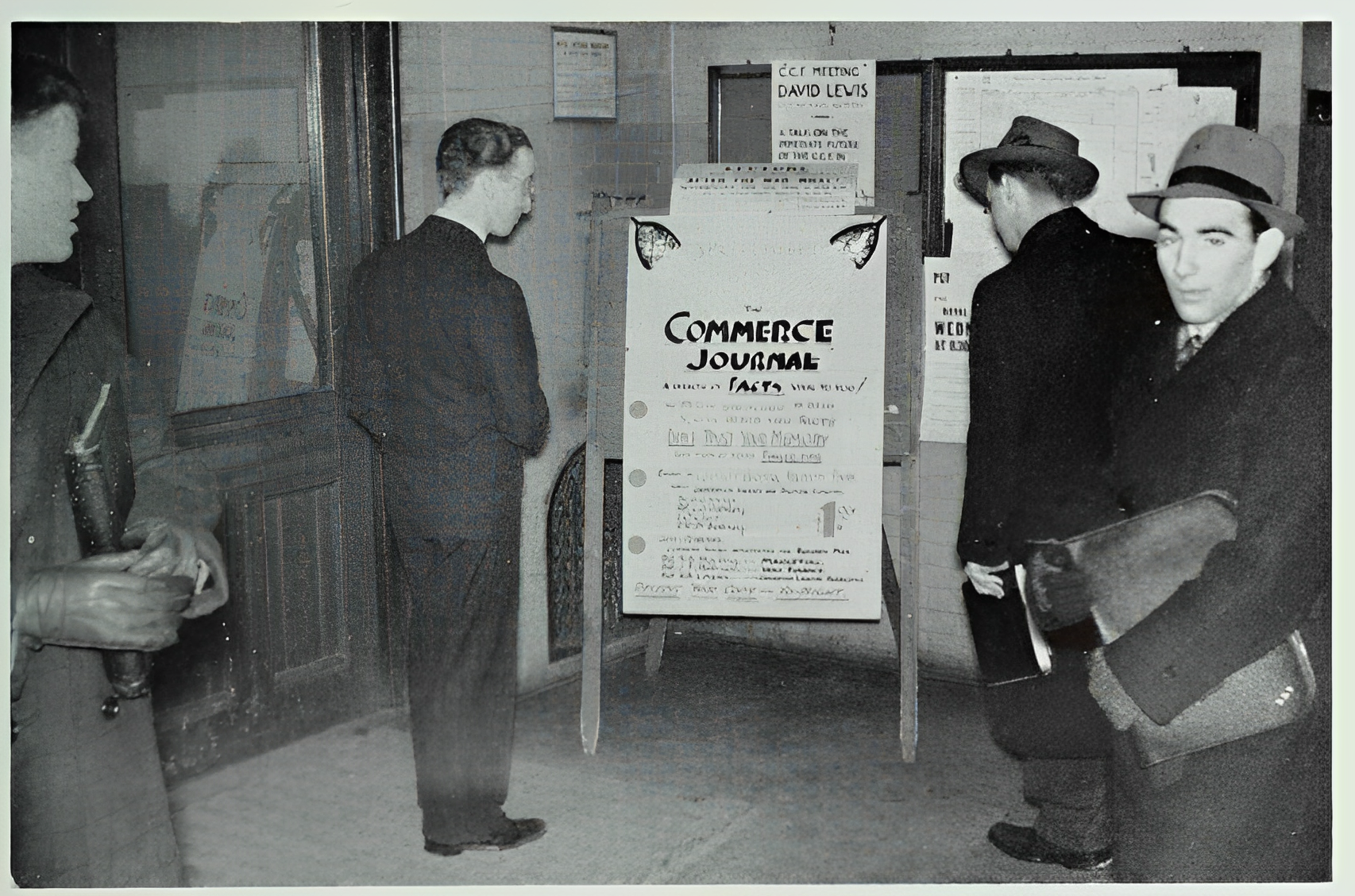 Black and white photo of people looking at a poster.