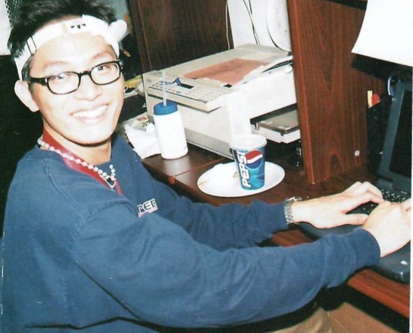 A commerce student using a laptop at a desk while smiling.