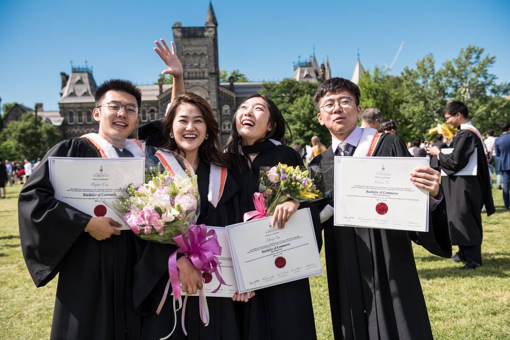 Four smiling people wearing graduation gowns and holding certificates.