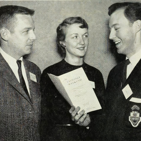 Black and white photo of one man, one woman and one man holding a brochure.