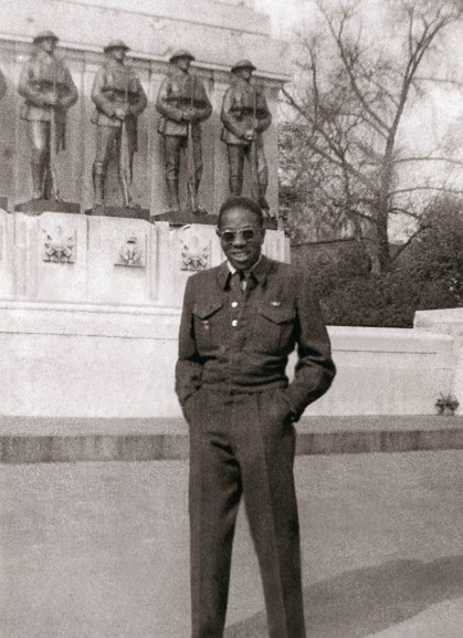 Black and white photo of man in suite in front of a solider memorial.
